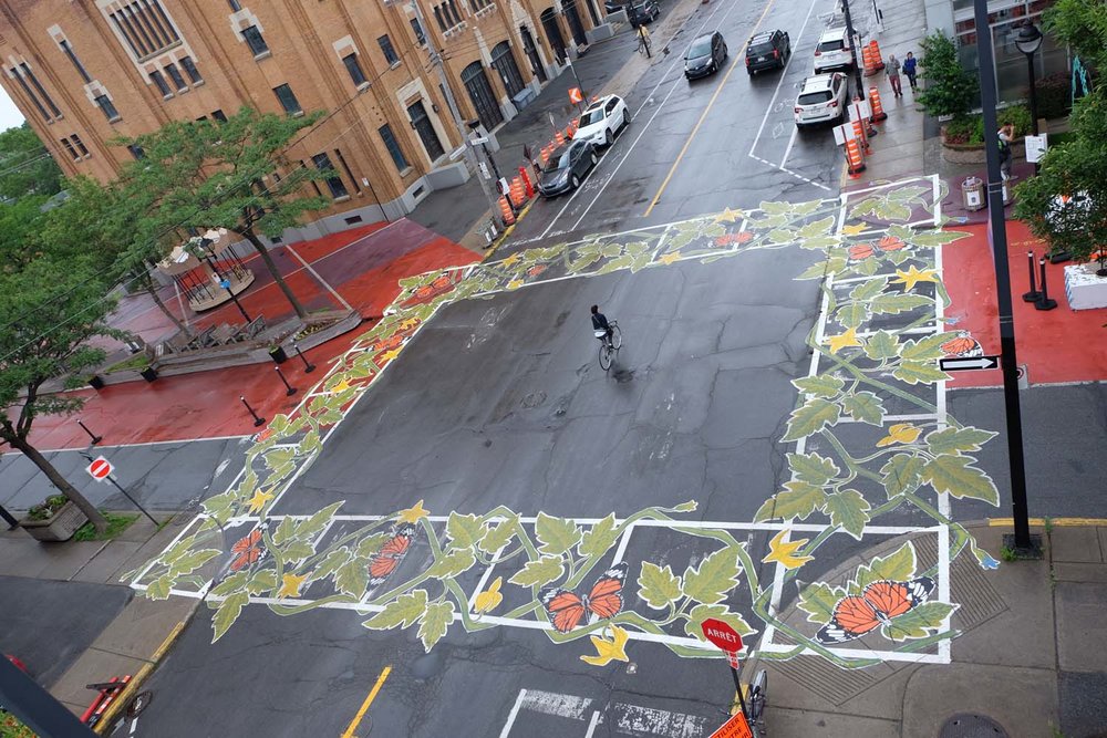 Foto aérea de uma esquina onde foram pintadas folhas como se fossem as 4 faixas de pedestres.
